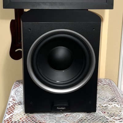Paradigm PDR-10 v.4 powered subwoofer with grille off, showing the 10-inch black cone with its silver trim ring and the Paradigm badge below